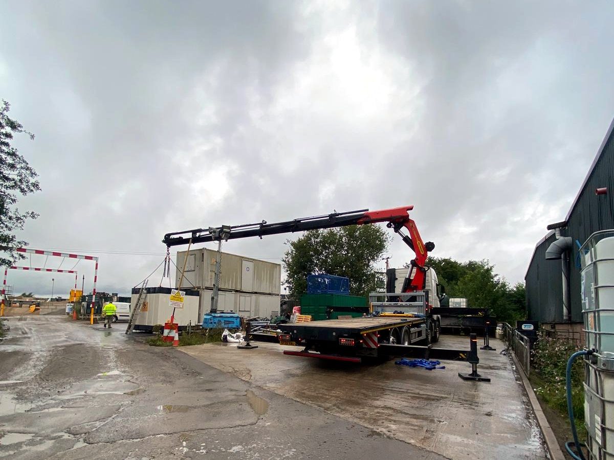 Heavy haulage lift on a muddy working site — red HIAB crane extended over the load.
