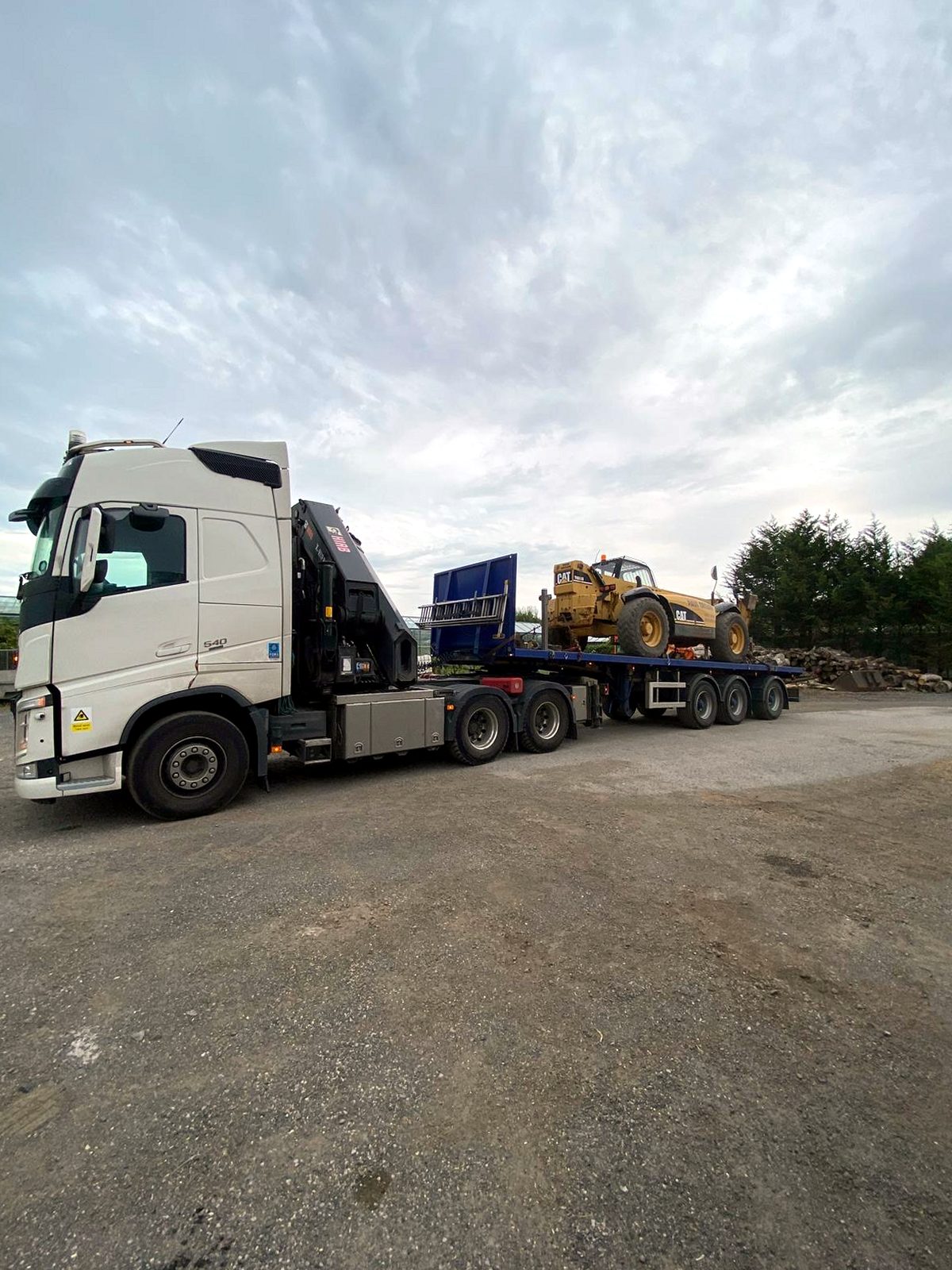 HIAB crane lifting a large crate from a flatbed at a delivery site.