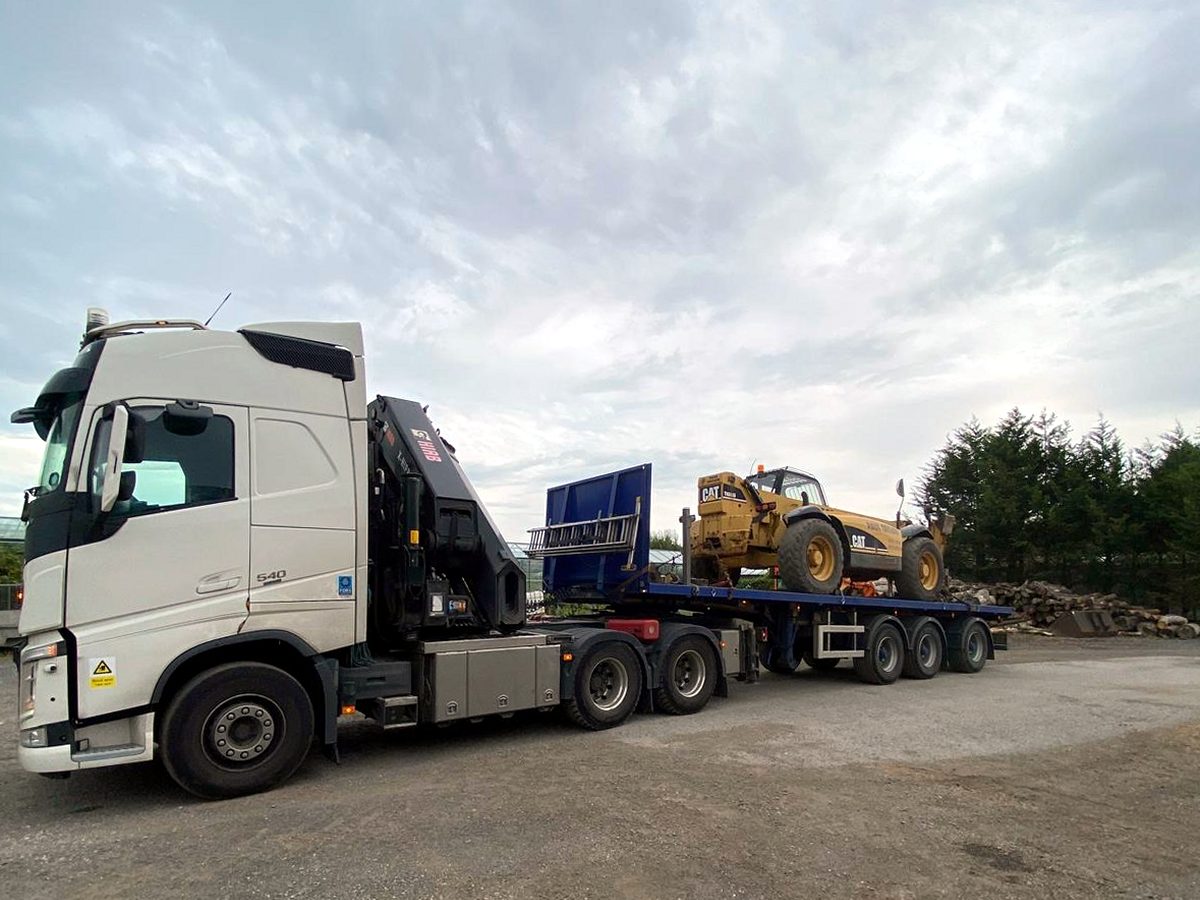 HIAB crane lifting a large crate from a flatbed at a delivery site.