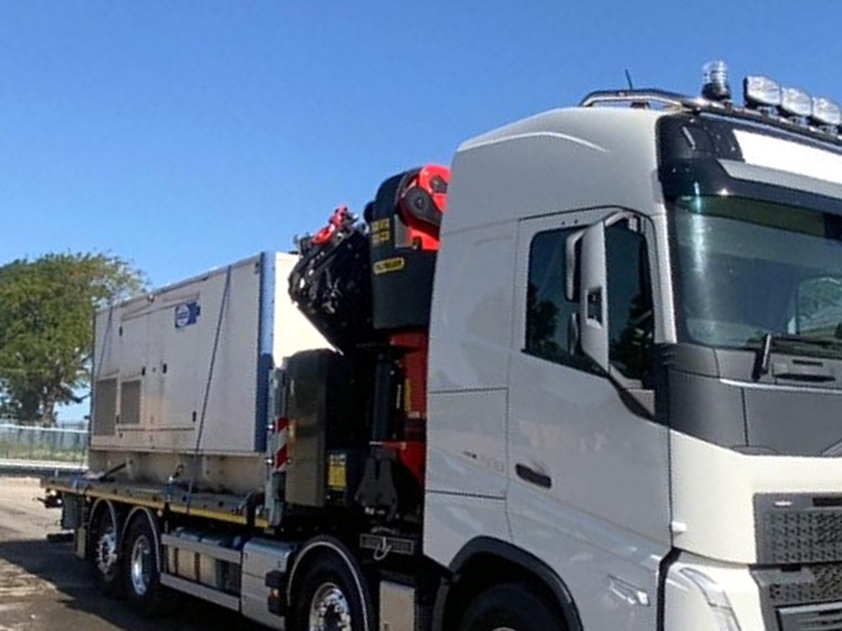 Blue-cab HIAB rig travelling between jobs on a quiet rural road.