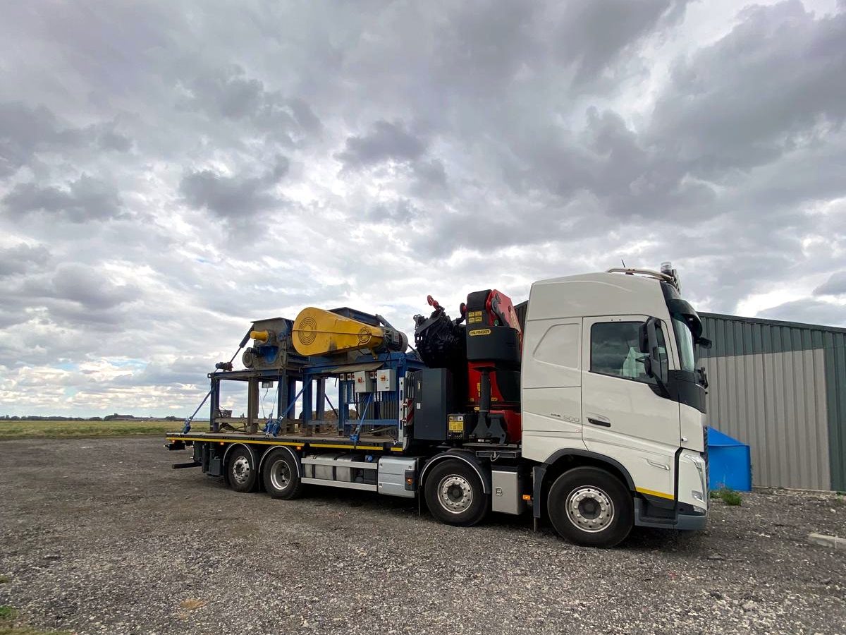 Bright-yellow plant machinery loaded onto an AC Lifting HIAB.