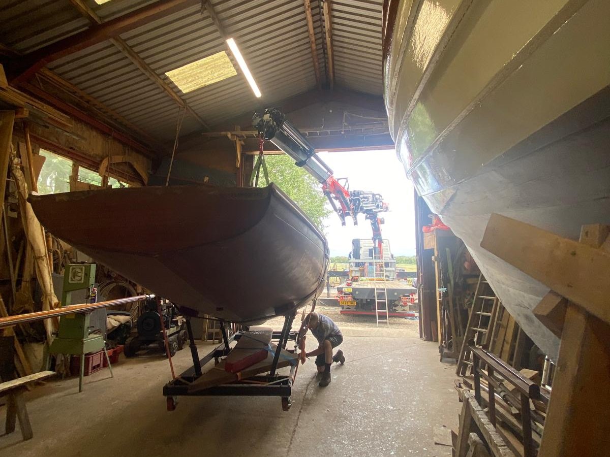 AC Lifting crane handling a classic wooden yacht inside a boat shed.