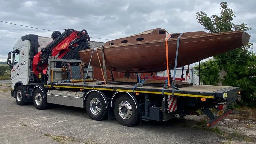 Restored classic wooden boat secured on an AC Lifting flatbed for transport.