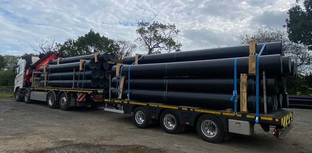 AC Lifting lorry and trailer loaded with large-diameter HDPE pipe.