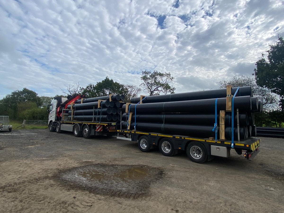 AC Lifting lorry and trailer loaded with large-diameter HDPE pipe.
