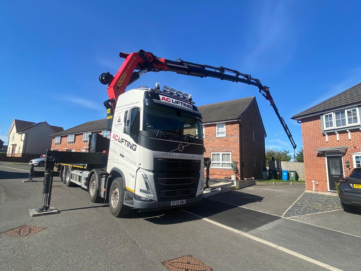 AC Lifting HIAB with boom extended on a residential street under blue sky.