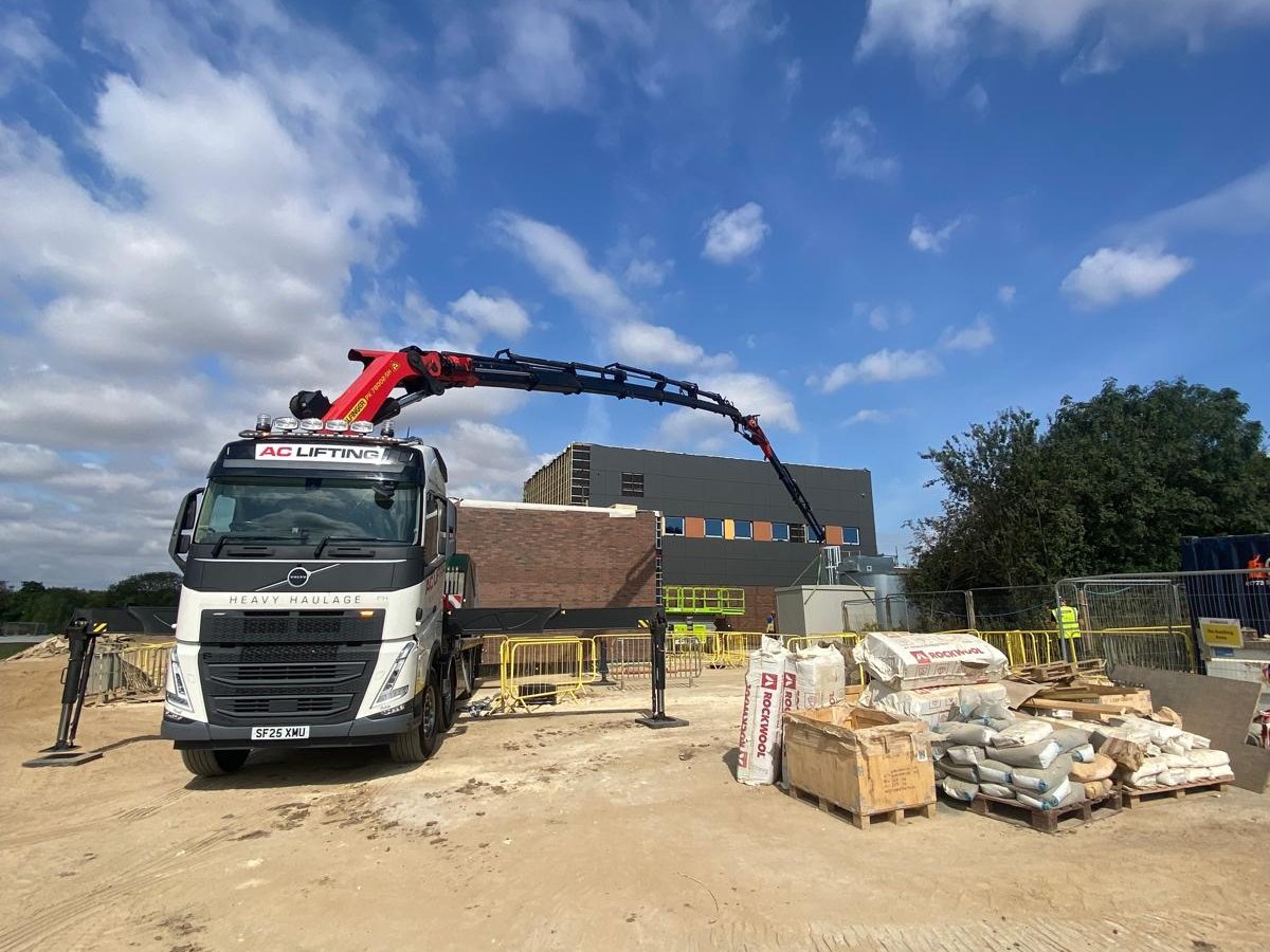 AC Lifting HIAB on a construction site alongside stacked building materials.