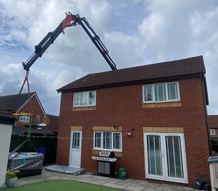 AC Lifting HIAB crane reaching over a house to place a load in the rear garden.