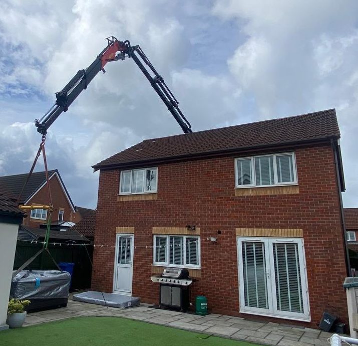 AC Lifting HIAB crane reaching over a house to place a load in the rear garden.