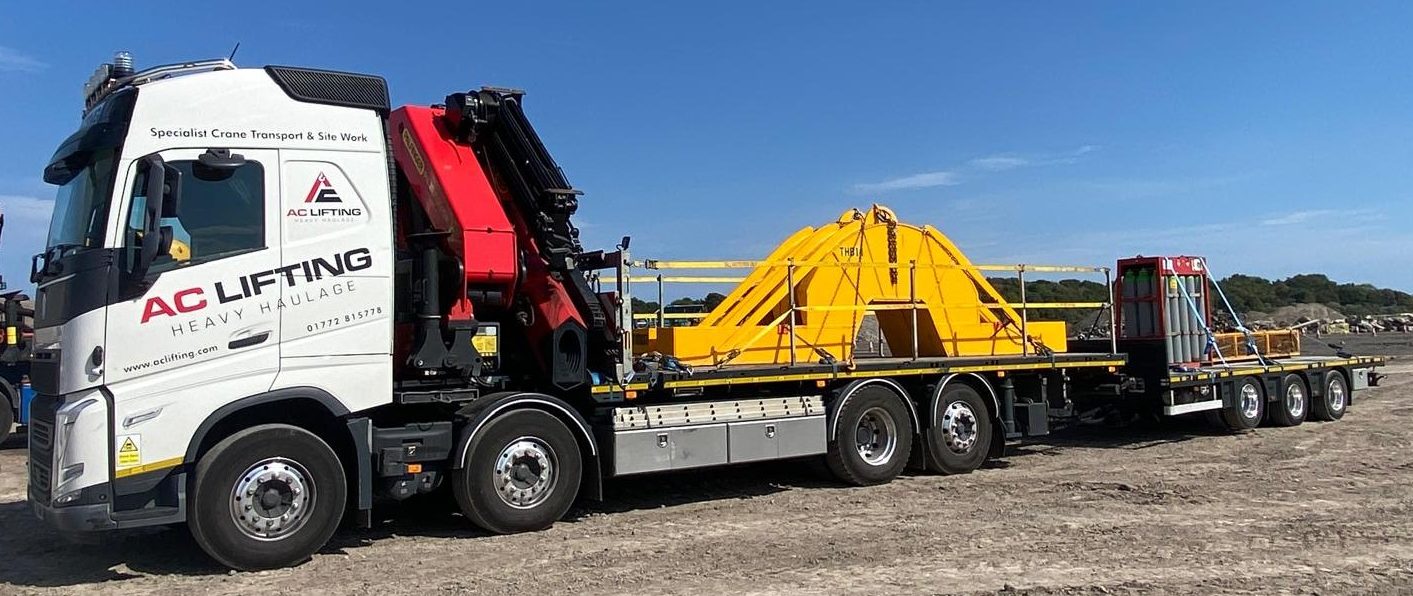 AC Lifting lorry and trailer loaded with large yellow plant equipment.
