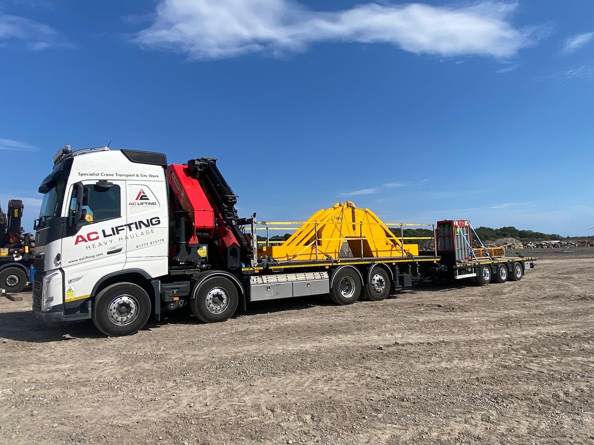 AC Lifting lorry and trailer loaded with large yellow plant equipment.